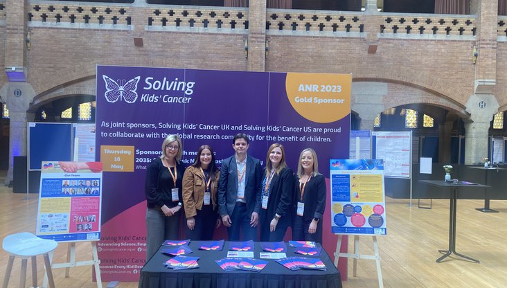 Research team stood at exhibition booth with informative banners and posters either side.